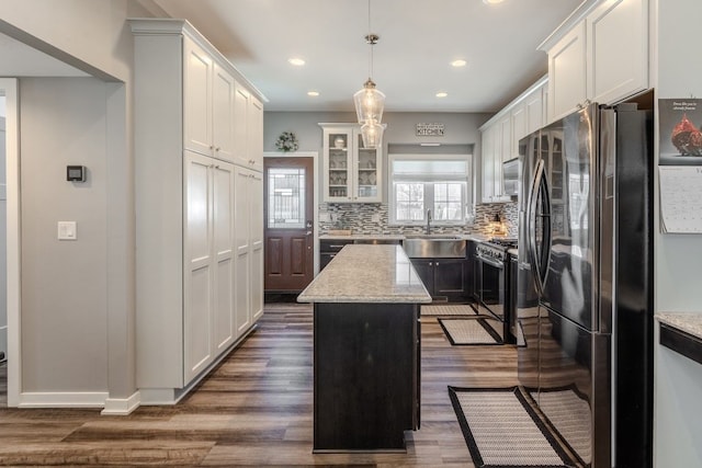 kitchen featuring backsplash, a kitchen island, dark wood-type flooring, appliances with stainless steel finishes, and a sink