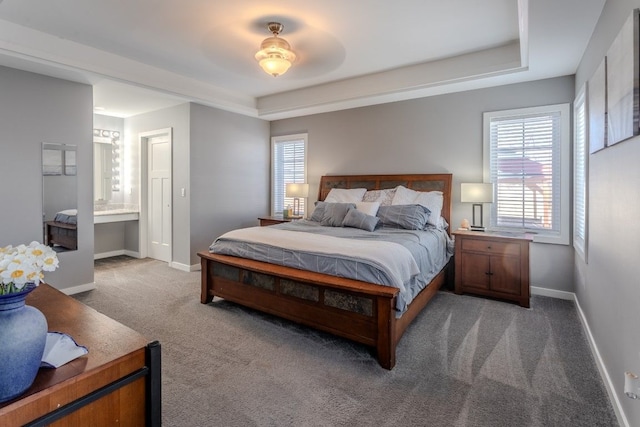 bedroom with a tray ceiling, baseboards, ensuite bathroom, and carpet flooring