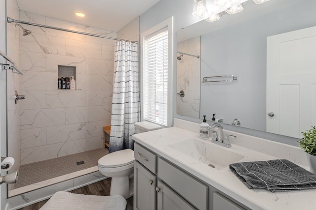 bathroom featuring vanity, toilet, wood finished floors, and a tile shower