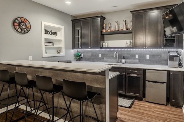 bar featuring indoor wet bar, tasteful backsplash, light wood-type flooring, and a sink