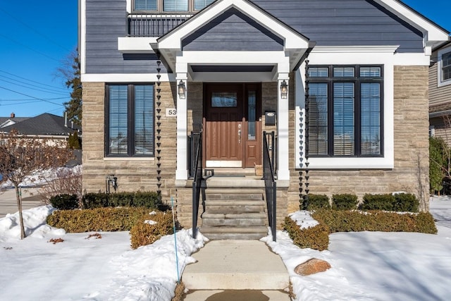 snow covered property entrance featuring stone siding