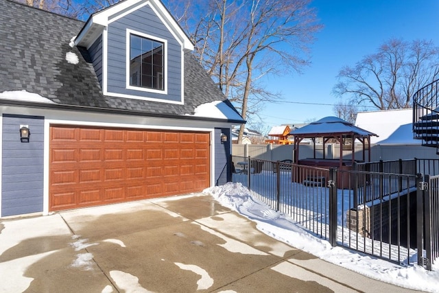 view of snowy exterior with a gazebo, a garage, fence, and a shingled roof