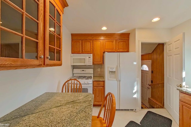 kitchen featuring recessed lighting, glass insert cabinets, brown cabinetry, light stone countertops, and white appliances