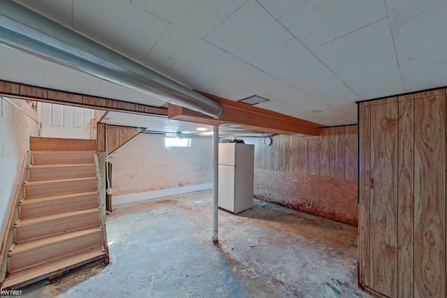 basement featuring wooden walls, stairs, and freestanding refrigerator