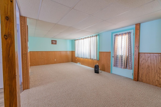 carpeted spare room with a wainscoted wall, wood walls, visible vents, and a drop ceiling