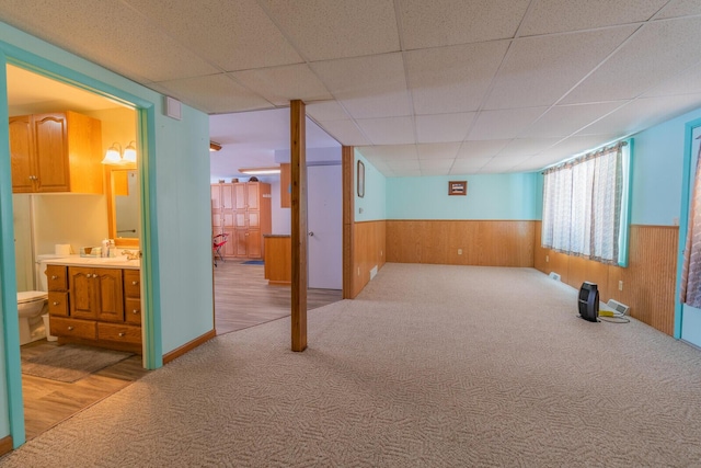 below grade area with a paneled ceiling, wooden walls, a wainscoted wall, carpet floors, and a sink