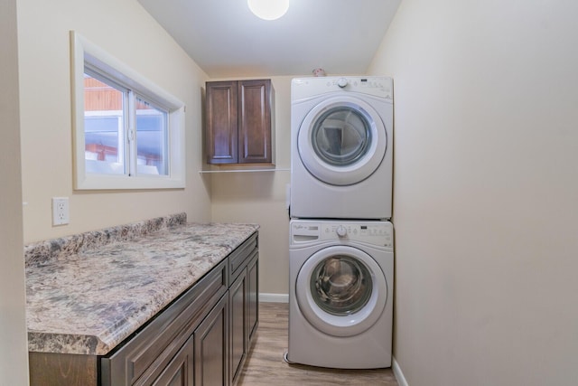 clothes washing area featuring stacked washer and clothes dryer, cabinet space, light wood-style flooring, and baseboards