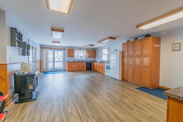 kitchen featuring white appliances, a sink, light wood-type flooring, brown cabinetry, and a wood stove