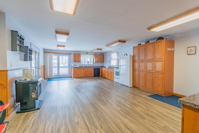 kitchen featuring brown cabinetry, white appliances, light wood-style floors, and a wood stove