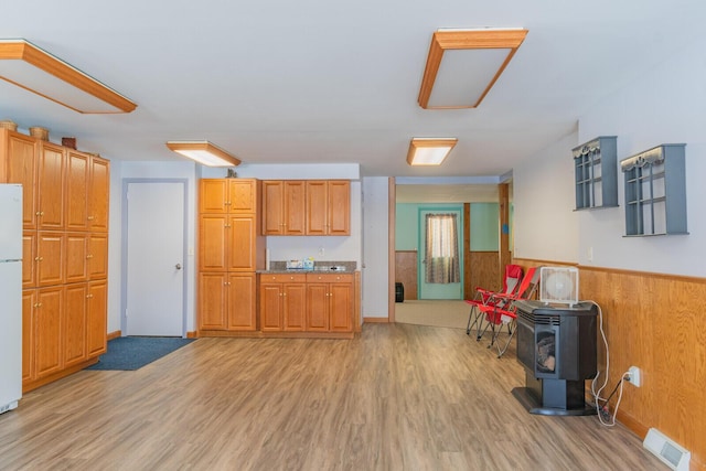 kitchen featuring light wood-style floors, a wood stove, wainscoting, and wood walls