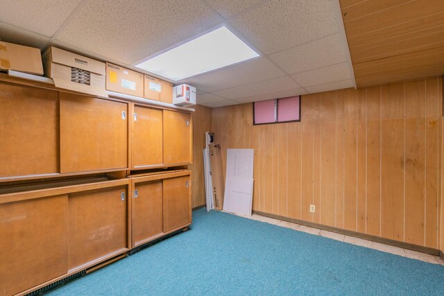 finished below grade area featuring wooden walls, a drop ceiling, and carpet flooring