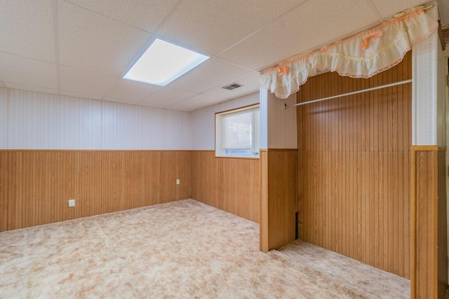 spare room featuring wood walls, visible vents, a drop ceiling, and a wainscoted wall