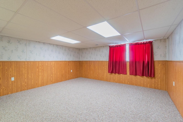 empty room featuring wainscoting, wood walls, carpet flooring, a drop ceiling, and wallpapered walls