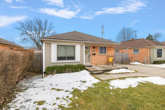 view of front of property featuring brick siding, roof with shingles, and fence