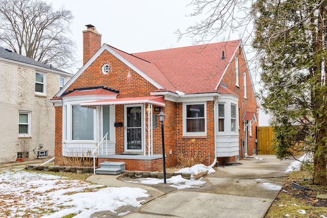 bungalow featuring a shingled roof, brick siding, fence, and a chimney