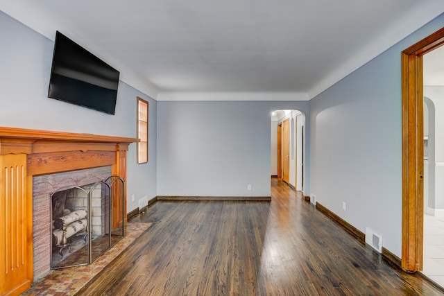 unfurnished living room featuring baseboards, a fireplace with flush hearth, arched walkways, and wood finished floors