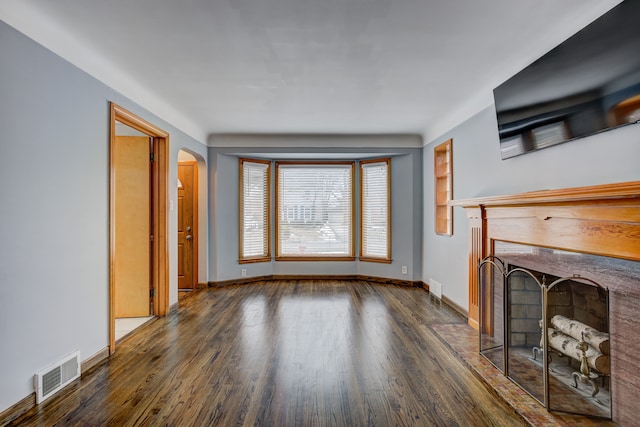 unfurnished living room featuring a fireplace with flush hearth, arched walkways, visible vents, and wood finished floors