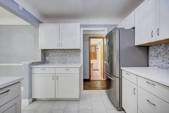 kitchen featuring light countertops, decorative backsplash, freestanding refrigerator, and white cabinets