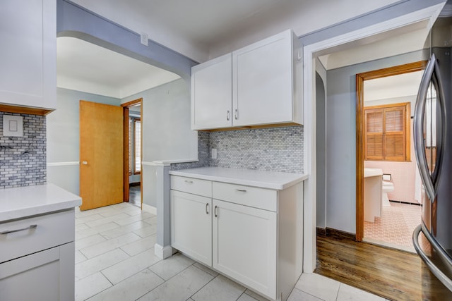 kitchen with white cabinets, light countertops, decorative backsplash, and freestanding refrigerator