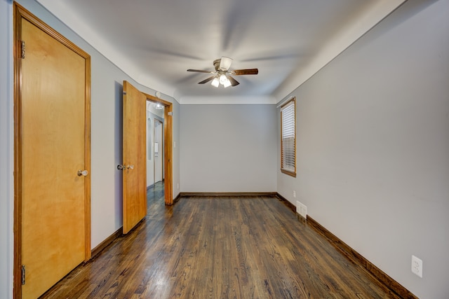 empty room featuring ceiling fan, dark wood finished floors, visible vents, and baseboards