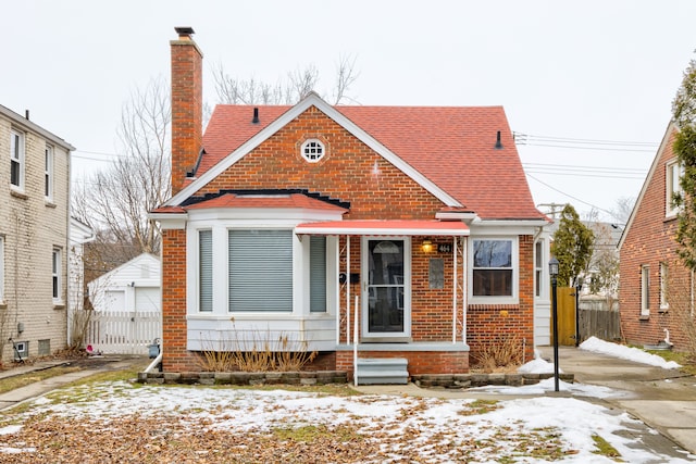 bungalow-style home featuring a garage, brick siding, fence, roof with shingles, and a chimney