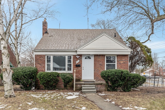 view of front of house featuring roof with shingles, brick siding, a chimney, and fence