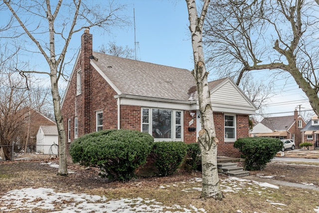 view of front facade featuring a shingled roof, a chimney, fence, and brick siding