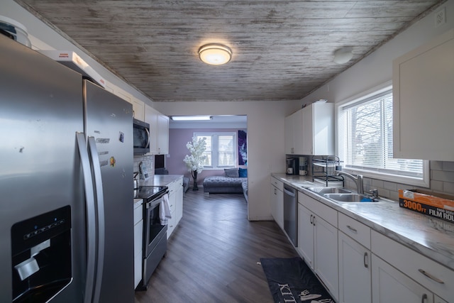 kitchen with wood finished floors, a sink, decorative backsplash, stainless steel appliances, and white cabinets