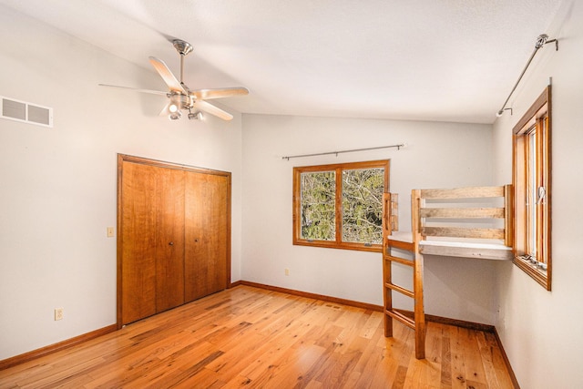 unfurnished bedroom with lofted ceiling, hardwood / wood-style flooring, baseboards, and visible vents