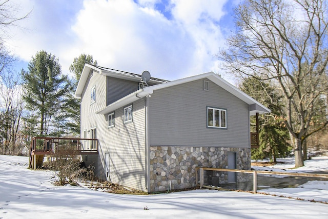 snow covered property with stone siding and a wooden deck