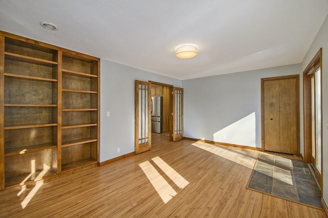 unfurnished bedroom featuring baseboards, visible vents, freestanding refrigerator, and light wood-style floors