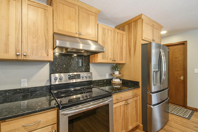 kitchen featuring light wood-style flooring, appliances with stainless steel finishes, dark stone countertops, under cabinet range hood, and light brown cabinets