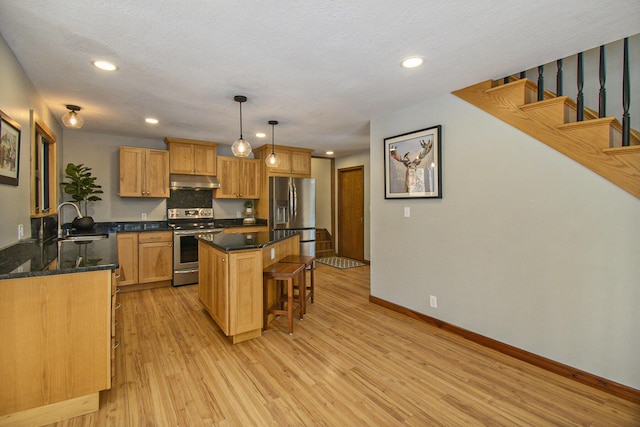 kitchen featuring a breakfast bar area, under cabinet range hood, a sink, appliances with stainless steel finishes, and light wood finished floors