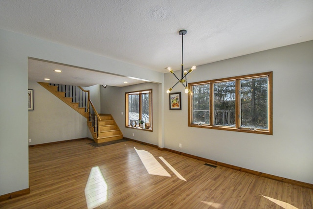 interior space with an inviting chandelier, a textured ceiling, wood finished floors, baseboards, and stairs