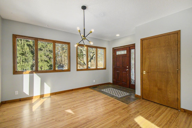 foyer featuring light wood-type flooring, an inviting chandelier, visible vents, and baseboards