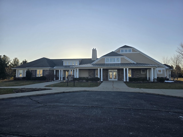 view of front facade featuring a standing seam roof, metal roof, a yard, stone siding, and a chimney