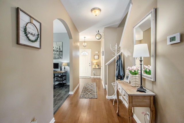 foyer featuring arched walkways, wood-type flooring, and baseboards