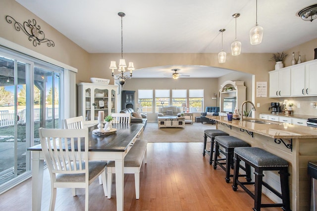 dining room with arched walkways, light wood finished floors, and ceiling fan with notable chandelier