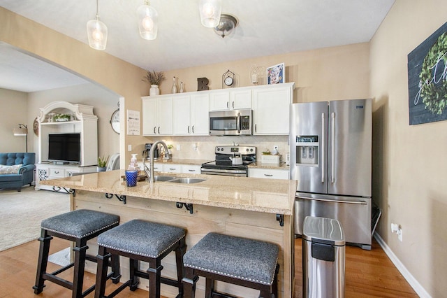 kitchen with stainless steel appliances, a sink, white cabinetry, tasteful backsplash, and a kitchen bar