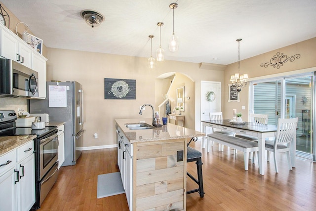 kitchen featuring arched walkways, stainless steel appliances, a sink, hardwood / wood-style floors, and an island with sink