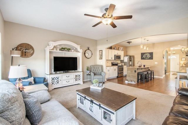 living room featuring baseboards, arched walkways, wood finished floors, carpet, and ceiling fan with notable chandelier