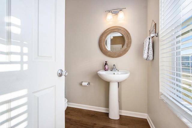 half bathroom featuring toilet, a sink, baseboards, and wood finished floors