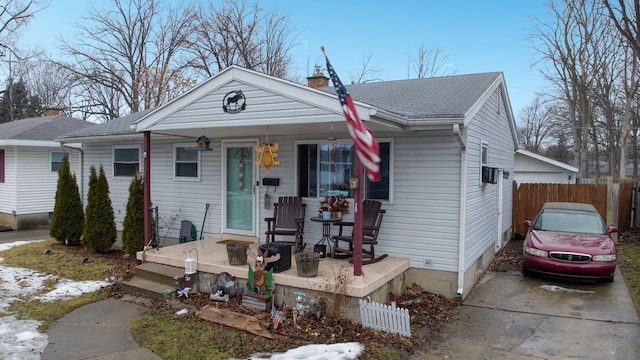 view of front facade featuring covered porch, a shingled roof, a chimney, and fence