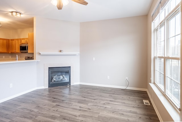 unfurnished living room with baseboards, visible vents, a tiled fireplace, ceiling fan, and wood finished floors