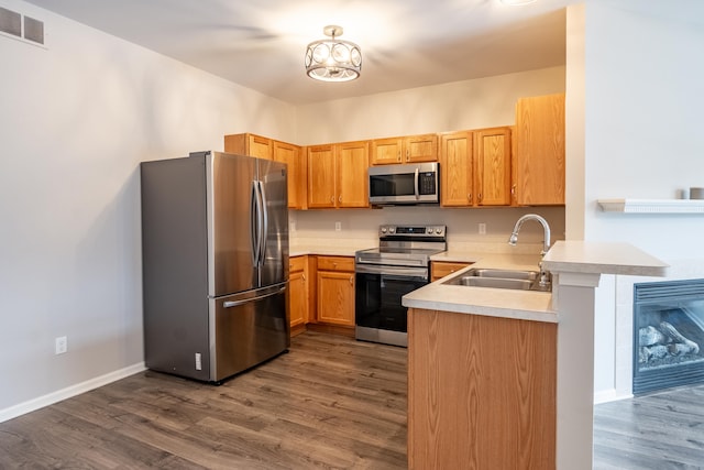 kitchen featuring a peninsula, dark wood-style flooring, a sink, visible vents, and appliances with stainless steel finishes