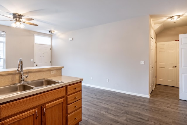 kitchen featuring dark wood finished floors, light countertops, brown cabinetry, a sink, and baseboards