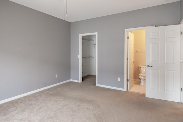 unfurnished bedroom with carpet floors, a closet, a spacious closet, ensuite bath, and baseboards