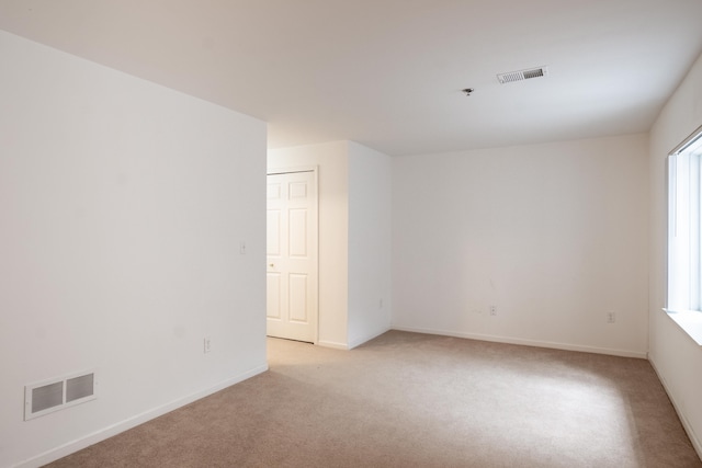 spare room with baseboards, visible vents, and light colored carpet