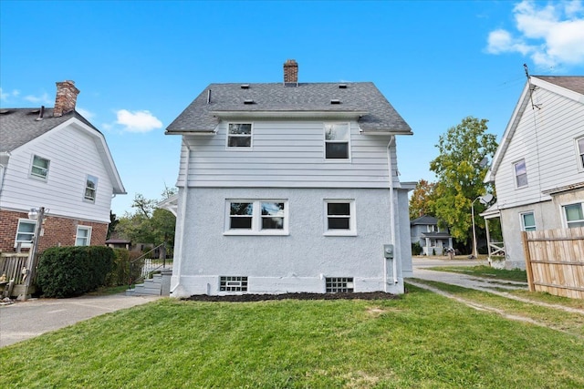 rear view of house with a shingled roof, a lawn, a chimney, fence, and stucco siding