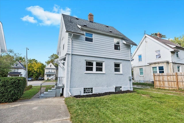 back of house with roof with shingles, a yard, a chimney, stucco siding, and fence